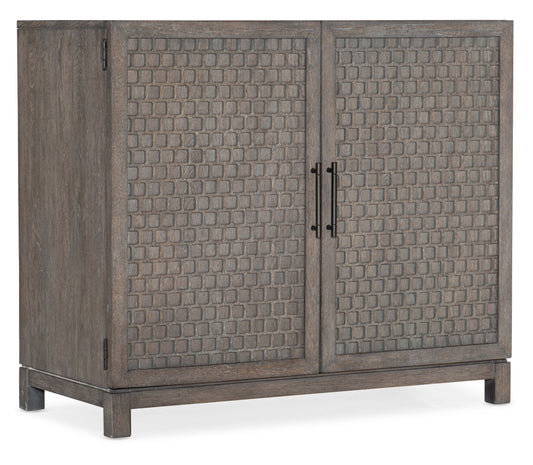 A wooden Hooker Furnishings 2-Door Chest with a medium wood finish features two doors with a textured, grid-like panel design and black metal handles, set against a white background.