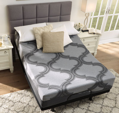 A neatly made bed featuring an Ashley Sleep® Hybrid 1100 mattress with a geometric-patterned comforter, set in a bright room with sliding glass doors, a gray headboard, and two white nightstands.